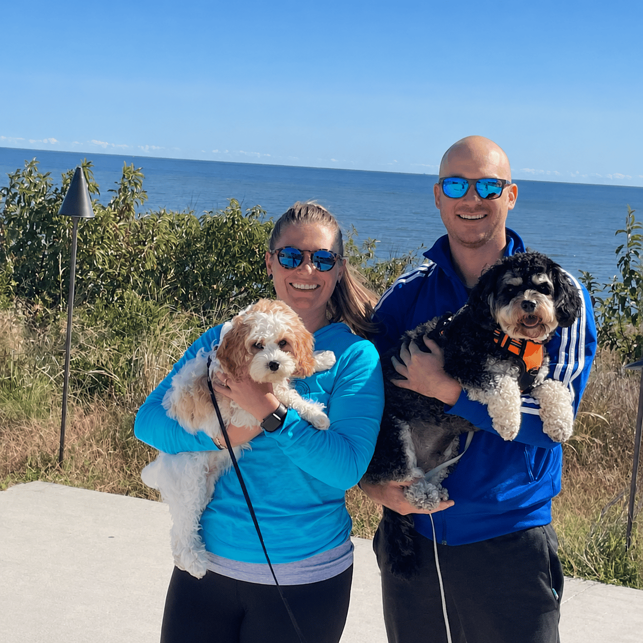 Danny and Nicole holding their two dogs, with the bay behind them