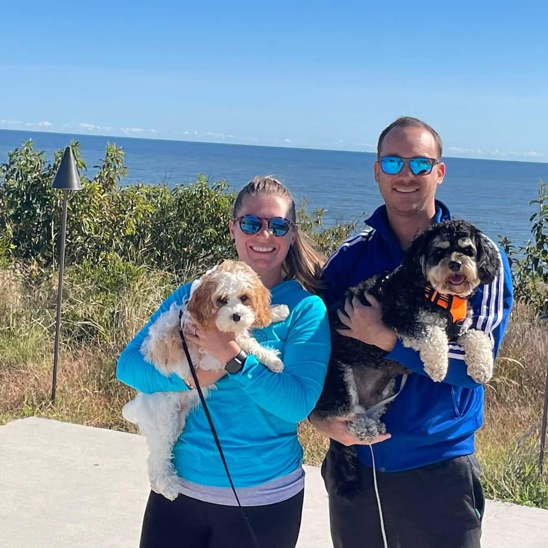 Danny and Nicole holding their two dogs, with the bay behind them